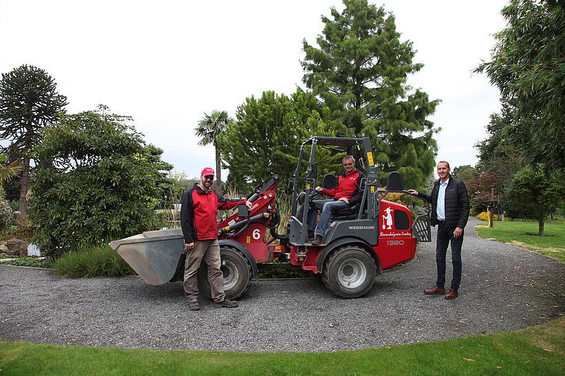 Zwei Männer stehen draußen vor einem Weidemann Hoftrac 1380 und ein Mann sitzt auf der Maschine