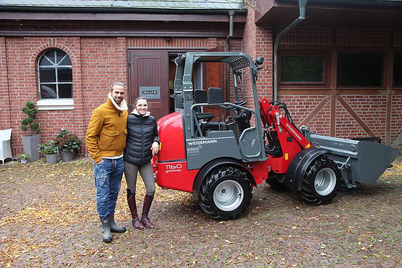 Eine Frau und ein Mann stehen draußen vor einem Weidemann Hoftrac 1160e