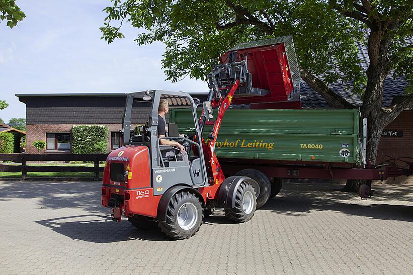 Ein Weidemann Hoftrac 1160e mit Fahrerschutzdach beläd einen Anhänder