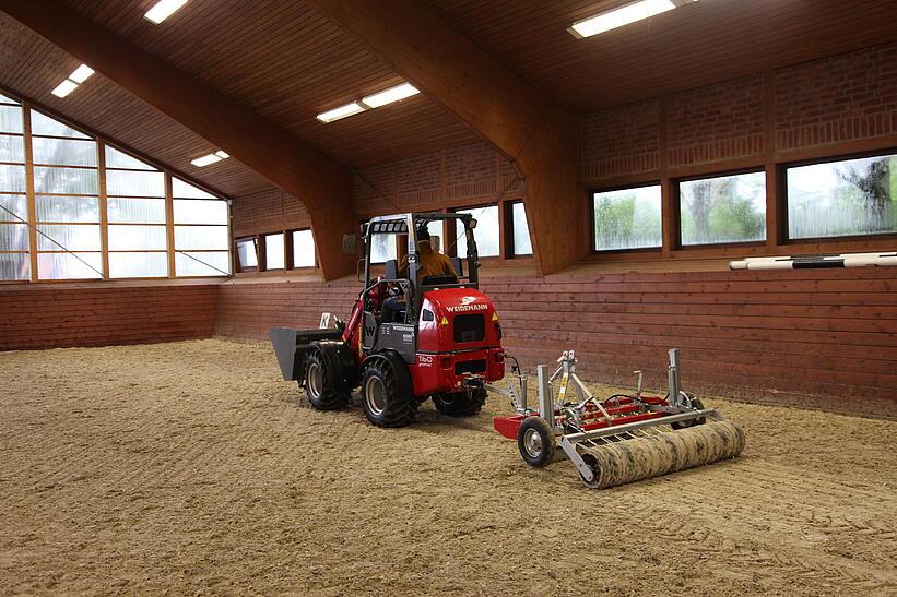 Weidemann Hoftrac 1160e in einer Reithalle mit Leichtgutschaufel und Reitplatz- und Bahnenplaner