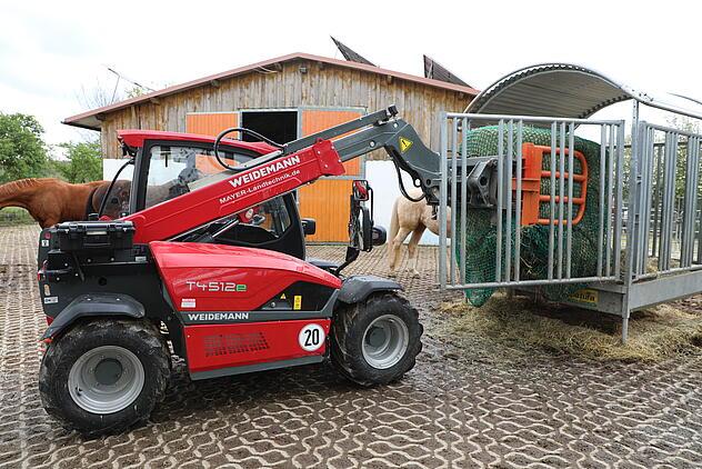 Weidemann Teleskoplader T4512e mit Rundballenzange im Einsatz auf einem Pferdehof