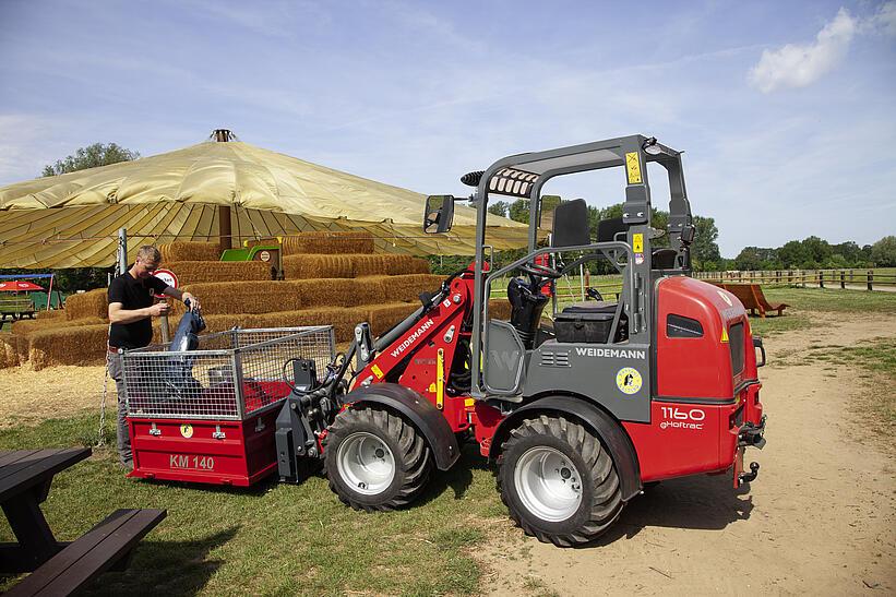 Ein Mann befüllt einen Container der an einem Weidemann Hoftrac 1160e befestigt ist