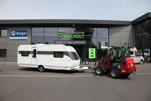 Weidemann Hoftrac 1280 mit Wohnwagen vor dem Gebäude beim Caravan Center Bocholt